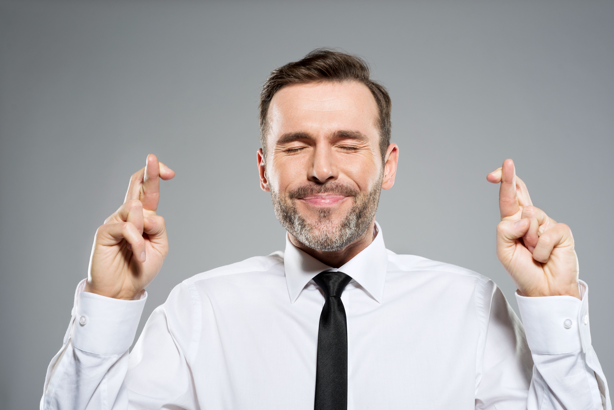 Portrait of businessman keeping his fingers crossed. Studio shot, grey background